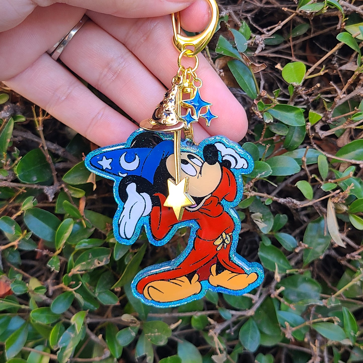 Colorful cartoon character keychain held by a hand with green foliage background