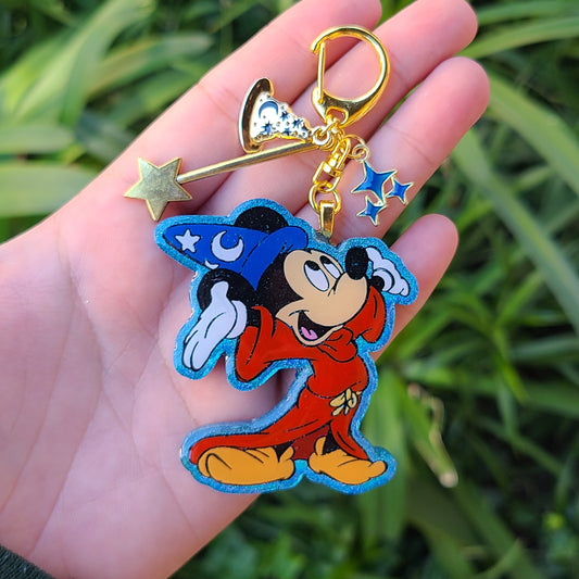 Keychain with cartoon character and star charms held in a hand against a grassy background